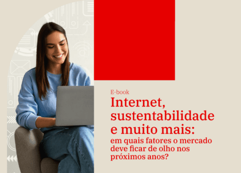 Mulher sorri ao digitar em um notebook. Ao lado, está escrito o texto: e-book Internet, sustentabilidade e muito mais: em quais fatores o mercado de investimentos deve ficar de olho nos próximos anos?