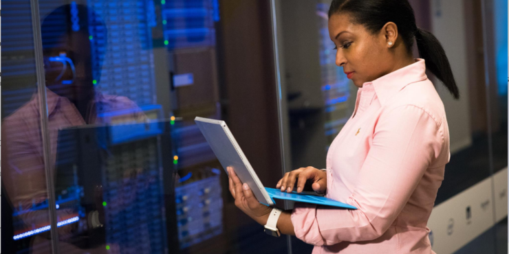 fintechs-infraestrutura-ti Uma mulher segura um notebook em frente à servidores de um data center.